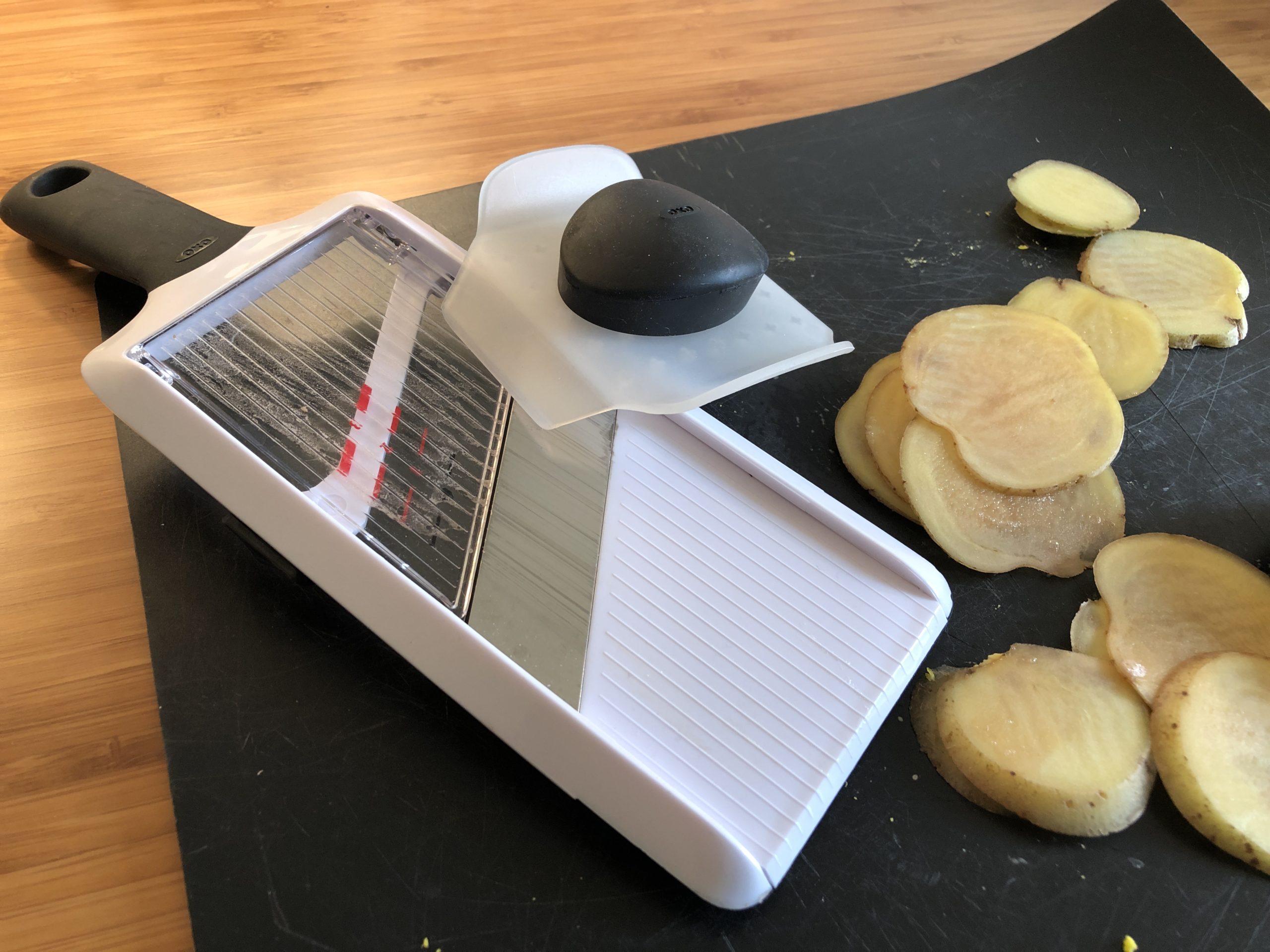 IMG-9069 Handled mandolin with guard and sliced potatoes onto of a black cutting board.