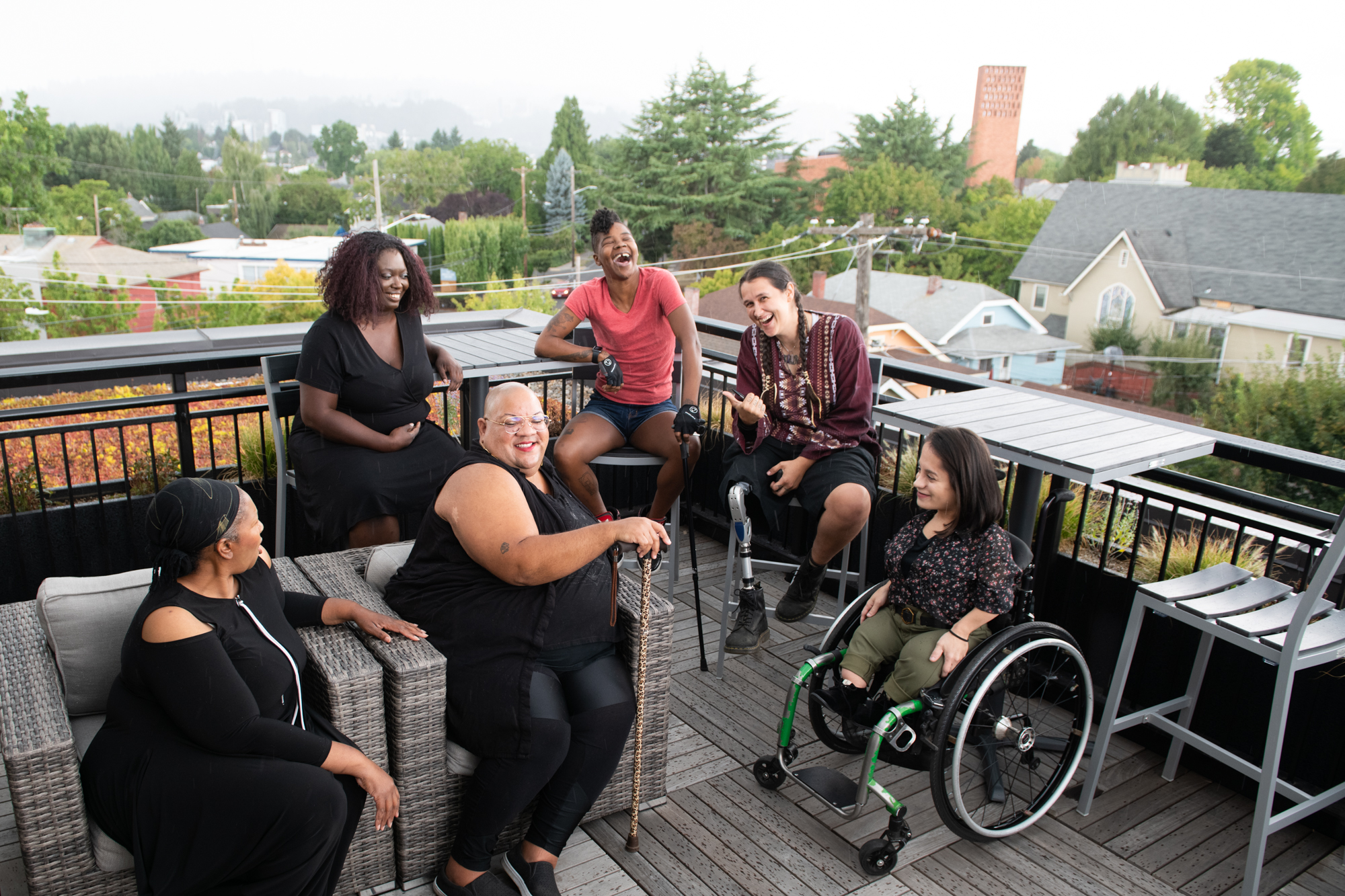 dah-party04 Overhead shot of six disabled people of color at a rooftop deck party. An Indigenous Two-Spirit person with a prosthetic leg smiles directly at the camera and gives a thumbs up while everyone else is engaged in conversation. Photo from Disabled And Here.