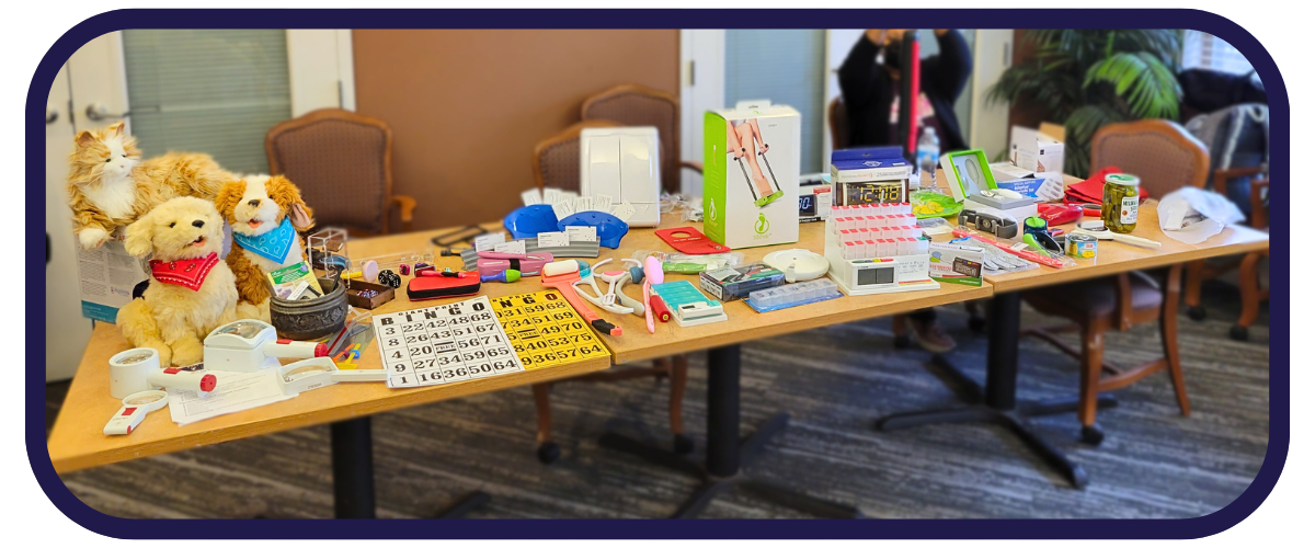at table long table with a large variety of different types of assistive technology ranging from companion pets, to large print bingo cards to sock aids and medication reminders