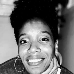 Feliece Black and white headshot of Feliece Turner, a Black woman with short black hair in an afro style. Feliece is sitting on steps with a plant behind her. Feliece is facing the camera with one hand on her chin and is smiling. She is wearing a t-shirt, cardigan and silver hoop earrings