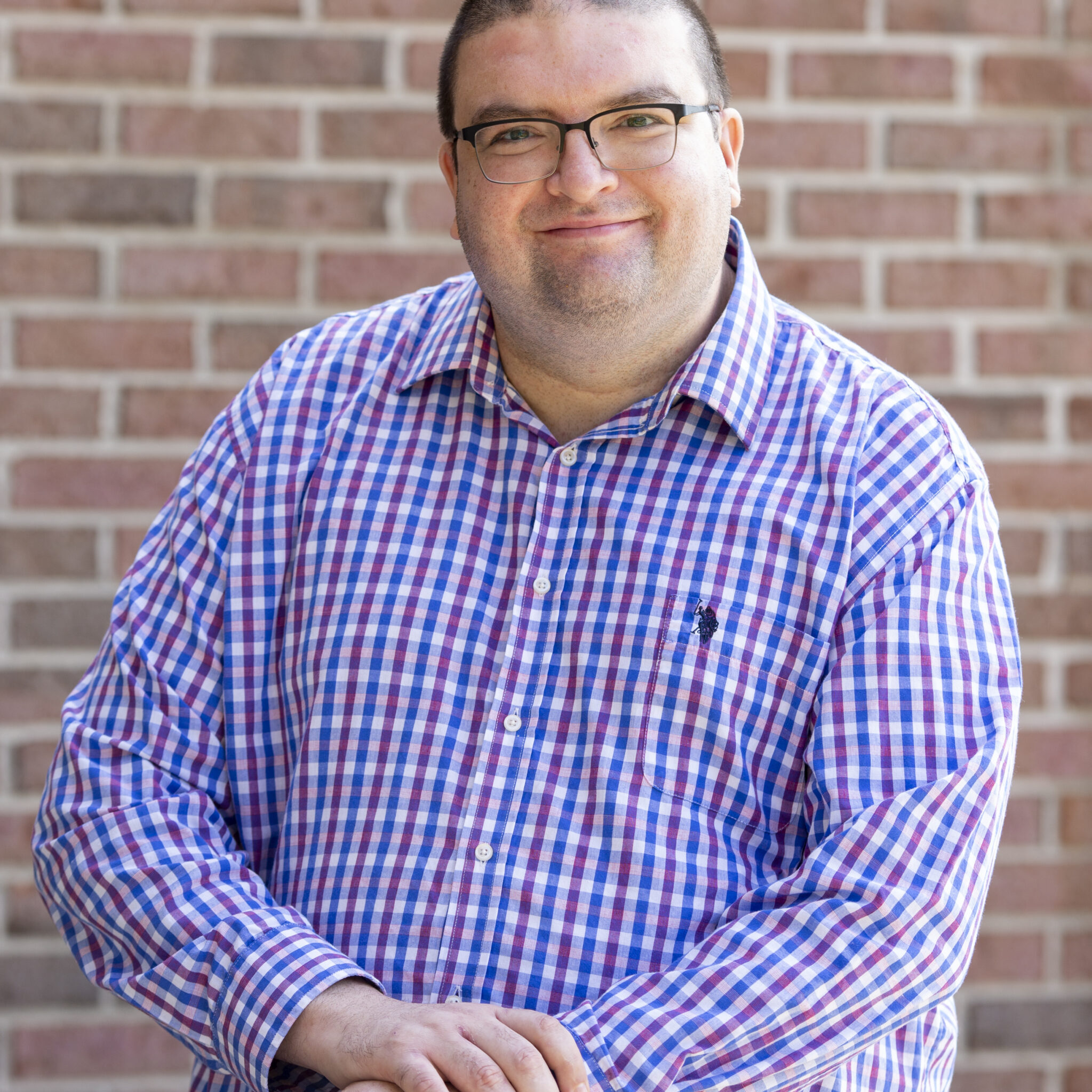 Frank Hispanic male with short brown hair in a blue and purple plaid collared shirt with glasses.
