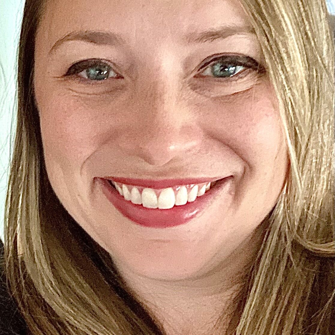 [Image description: Headshot of Janna Bitterle, a white woman with long brown hair and blue eyes. Janna is indoors with a blue and white wall behind her. She is looking directly at the camera, smiling. She is wearing a black sweater. End image description.] --